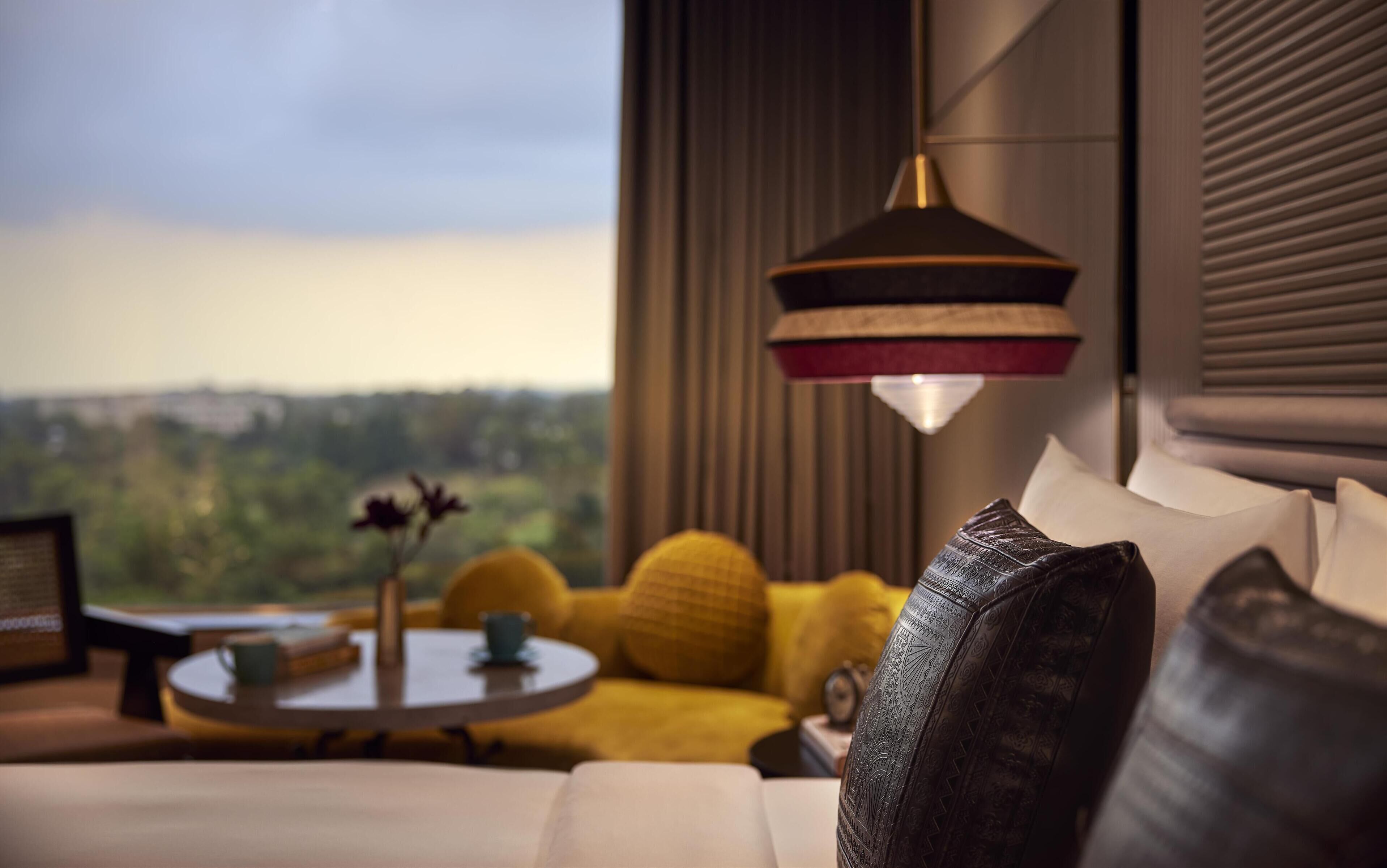 A modern bedroom with a large window, a round table with a vase, and a sofa with patterned pillows.
