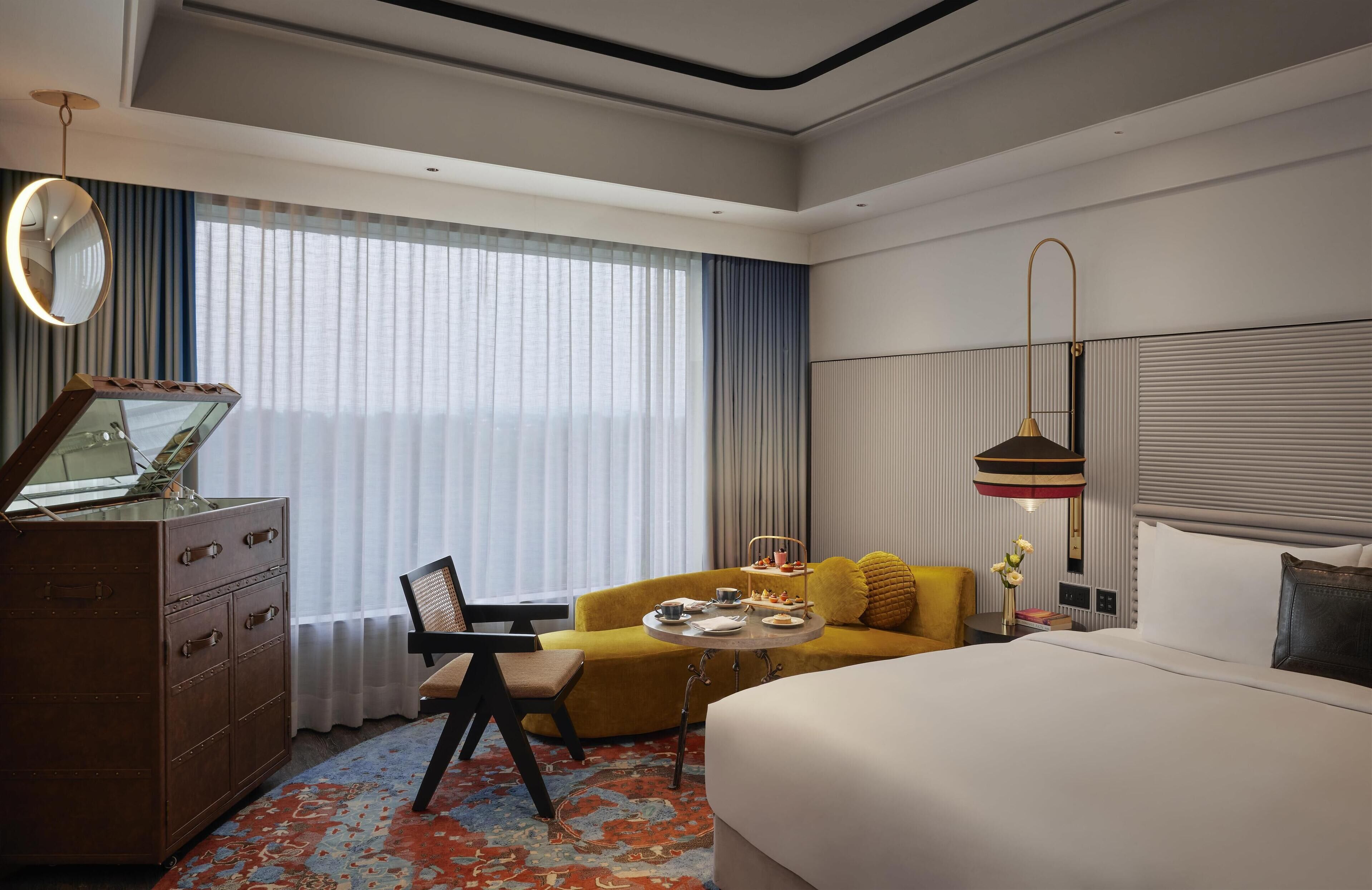 A hotel room with a bed, a sofa, a desk with a mirror, and a window with curtains.