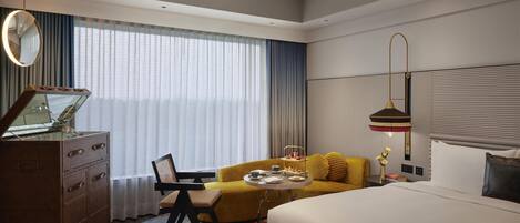 Una habitación de hotel con cama, sofá, escritorio con espejo y ventana con cortinas.