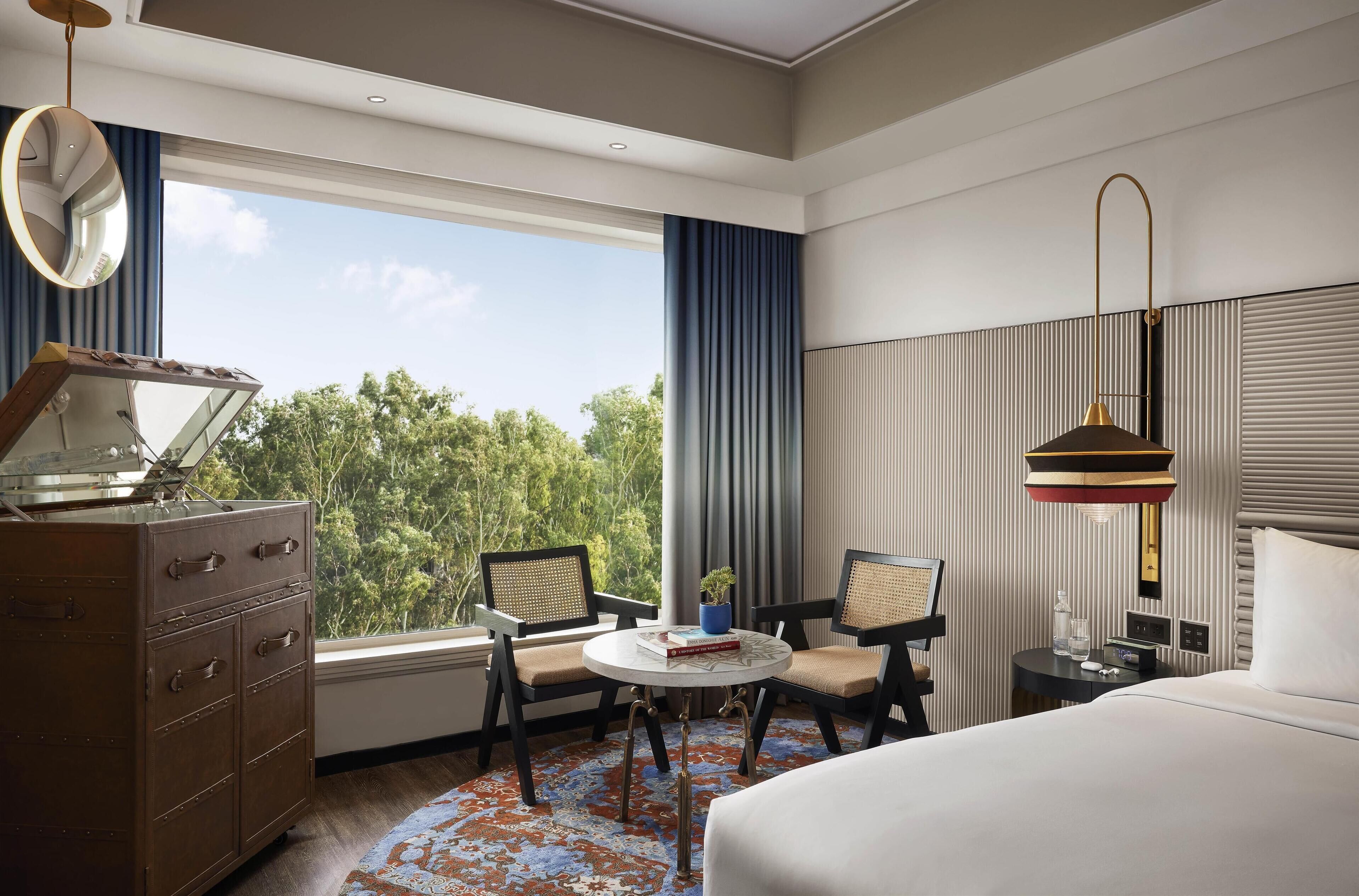 A hotel room with a large bed, a desk with a chair, a dresser, and a window with a view of trees.