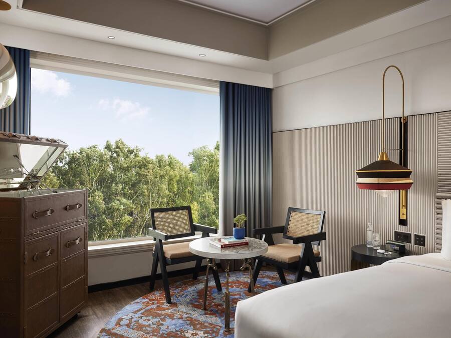 A hotel room with a large bed, a desk with a chair, a dresser, and a window with a view of trees.