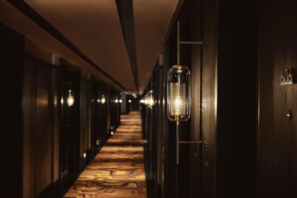A hotel hallway with a patterned carpet, wooden doors, and wall-mounted light fixtures. - Hyatt Centric Sector 17 Chandigarh (Chandigarh)