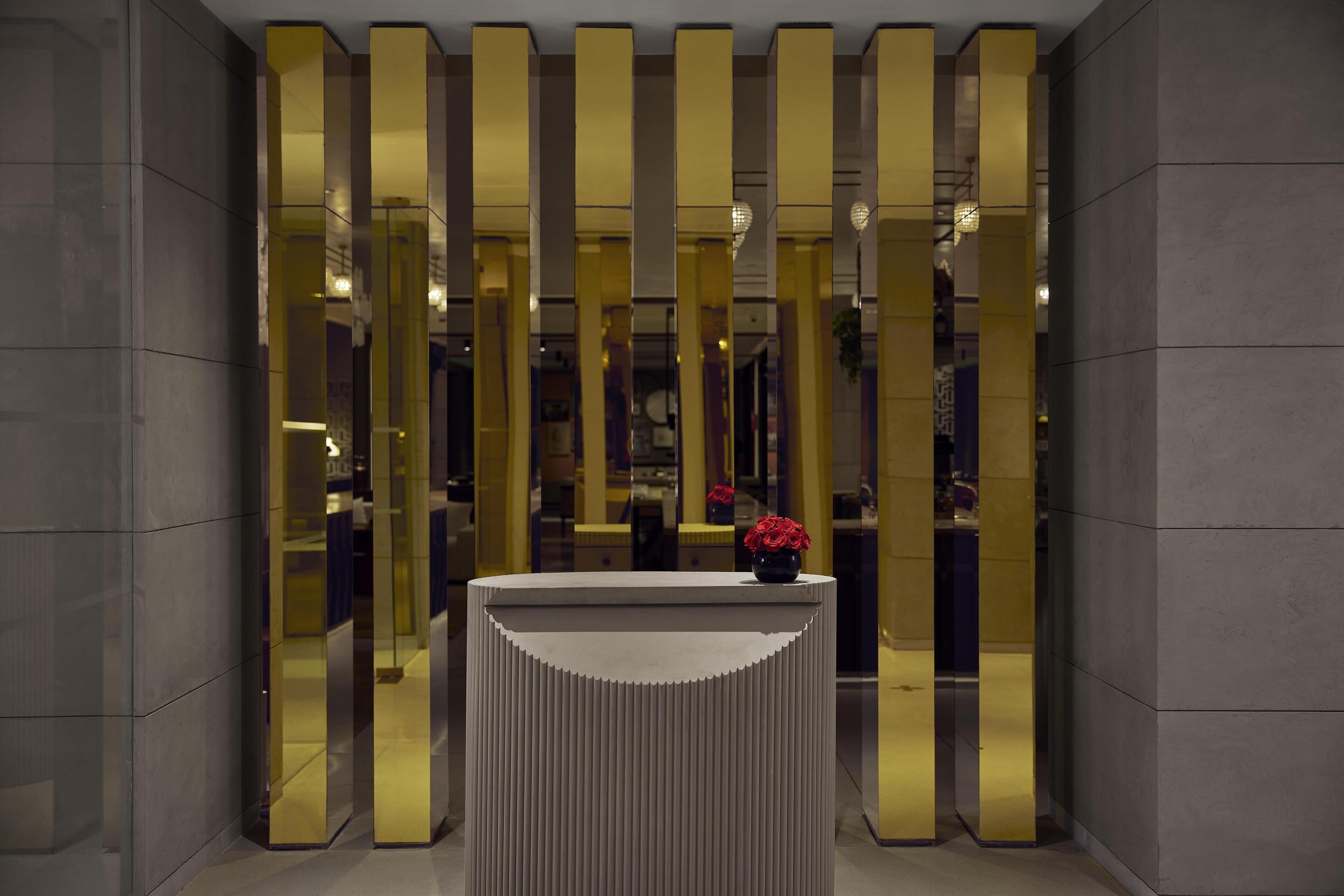 A reception area with a modern design, featuring a central console table with a vase of red flowers and vertical golden panels in the background.