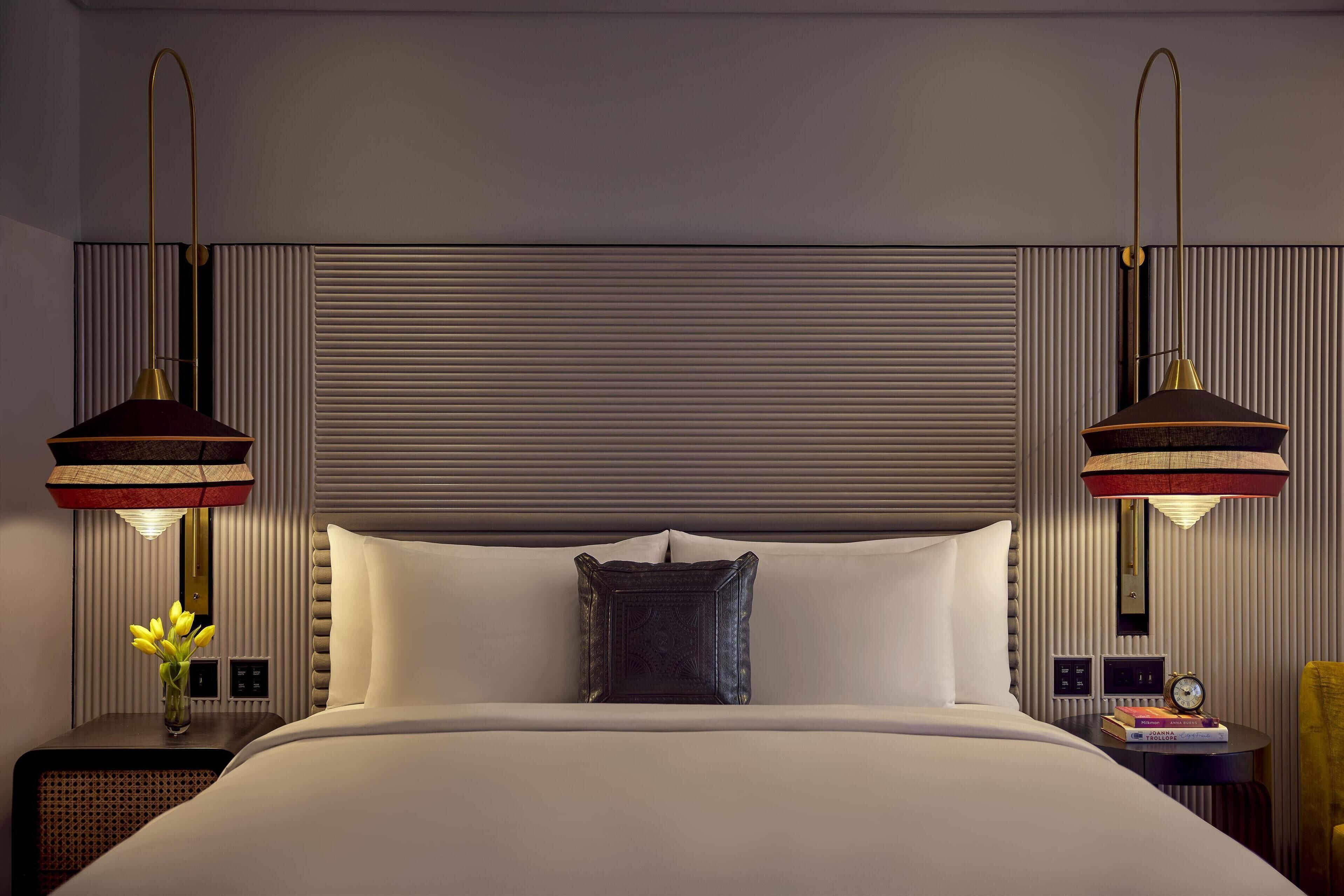 A hotel room with a large bed, two bedside tables with lamps, a nightstand, and a wall-mounted clock.
