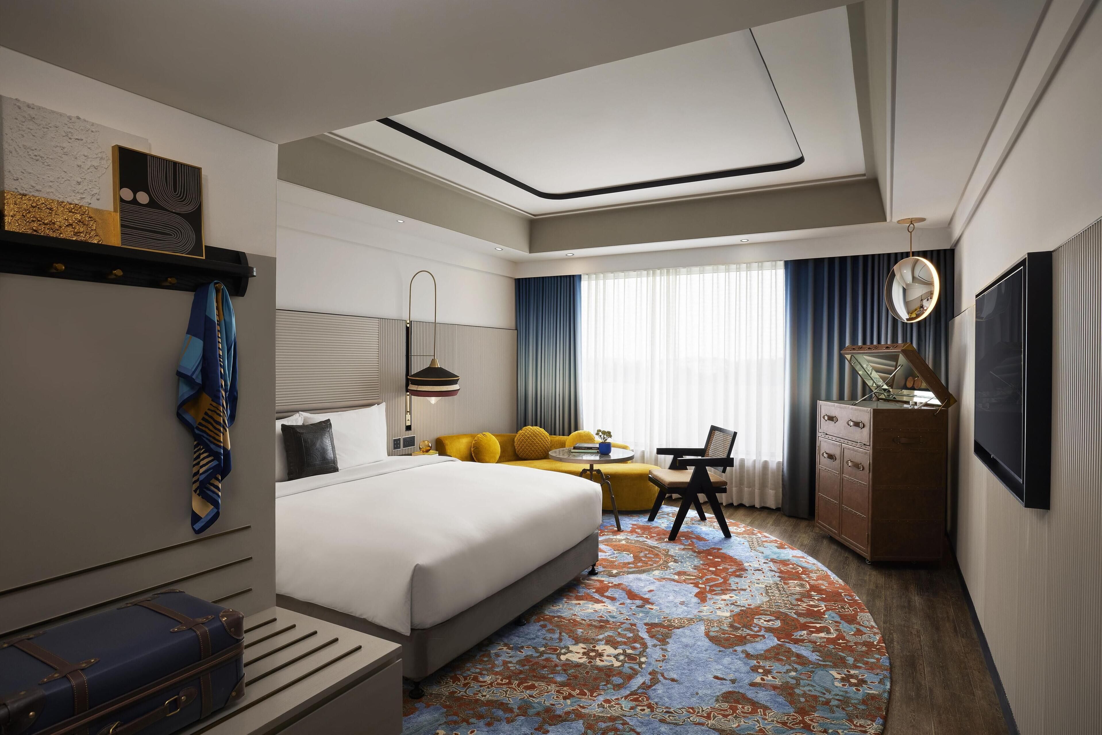 Quarto de hotel moderno com uma cama grande, um sofá, uma escrivaninha e um aparador.