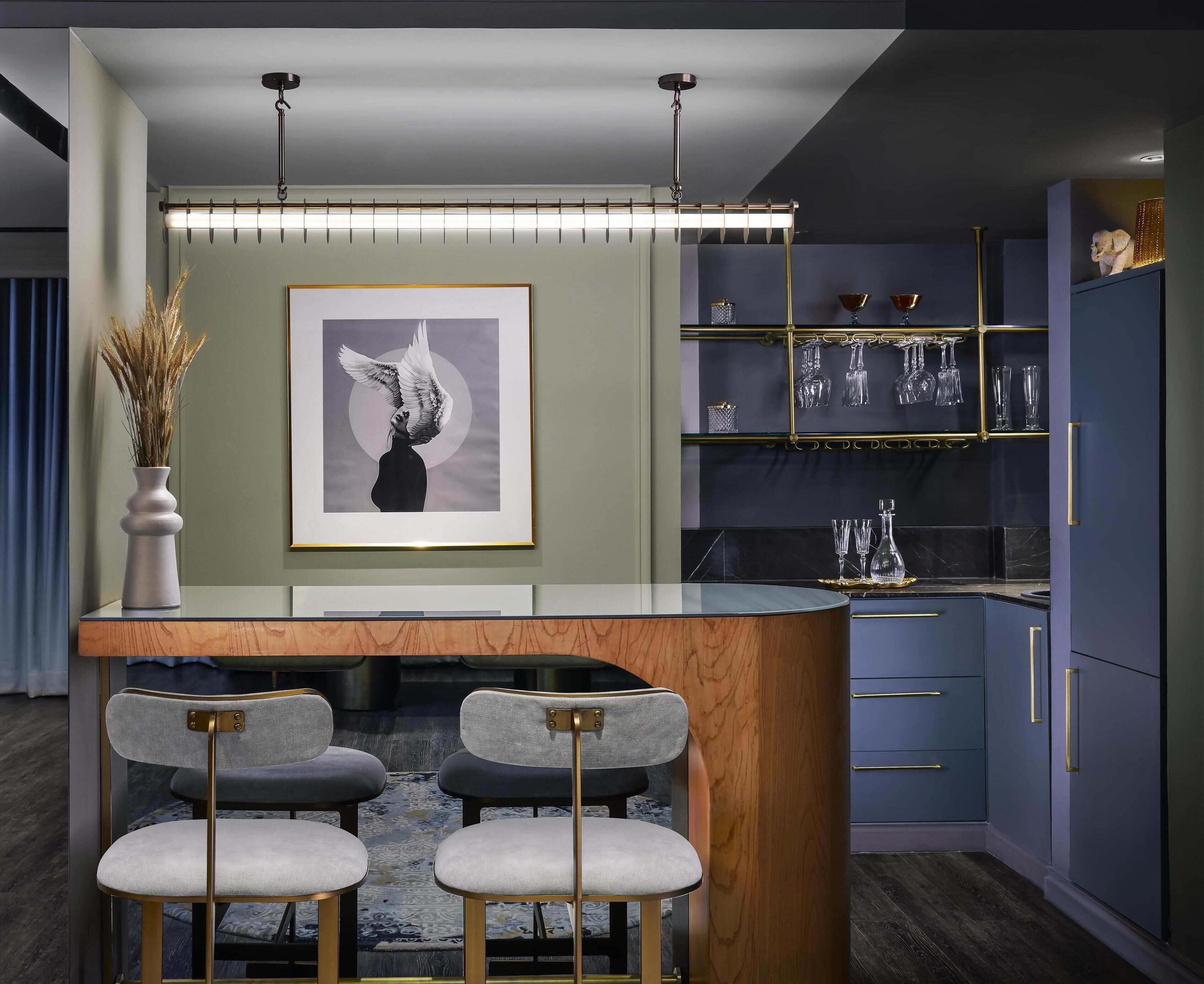 A modern kitchen with a central island, bar stools, a framed artwork, and glassware on shelves.
