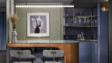 A modern kitchen with a central island, bar stools, a framed artwork, and glassware on shelves.
