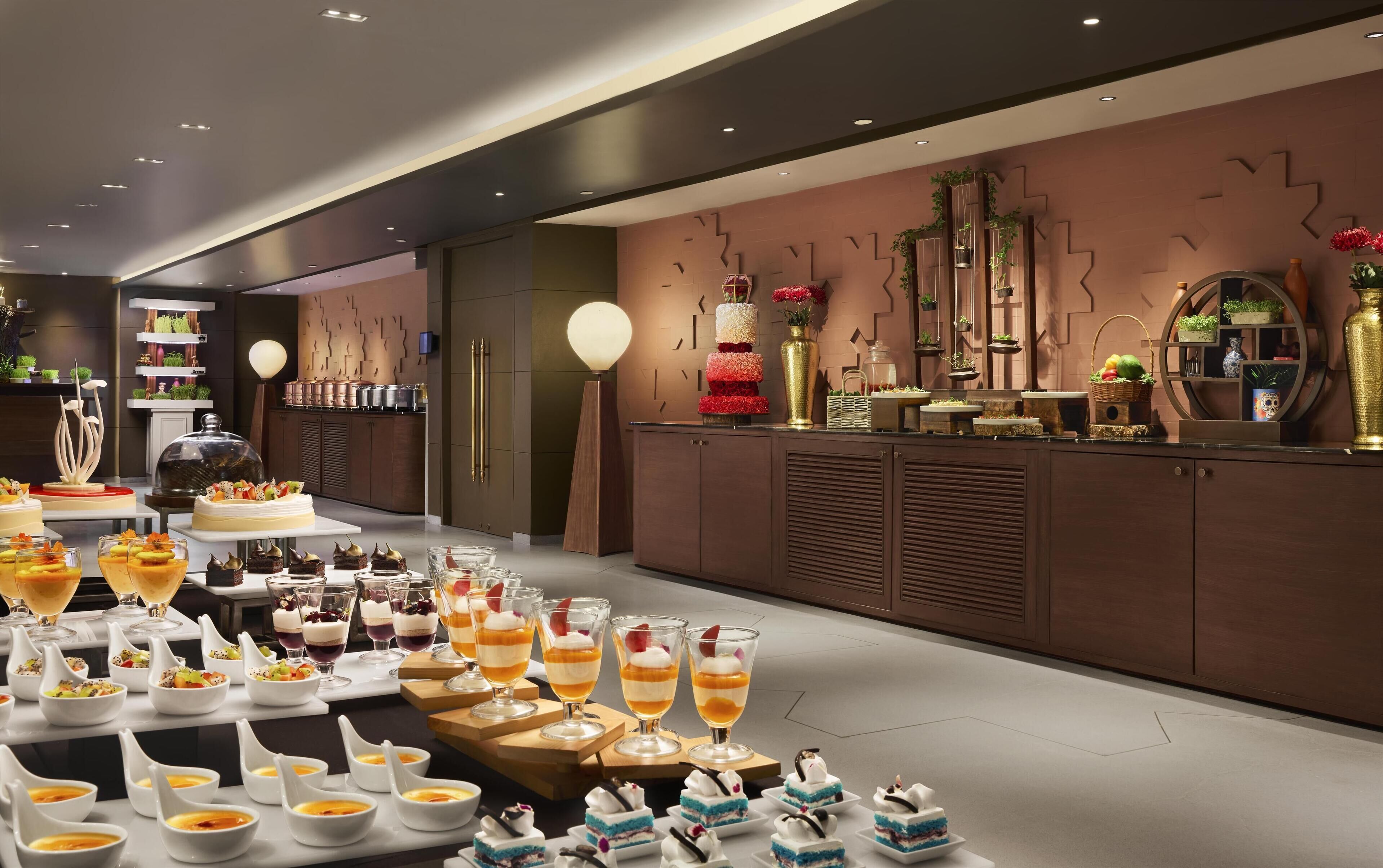 En moderne hotellobby med en lang receptionsdisk, en dekorativ væg med geometriske mønstre og et udvalg af desserter og drikkevarer.
