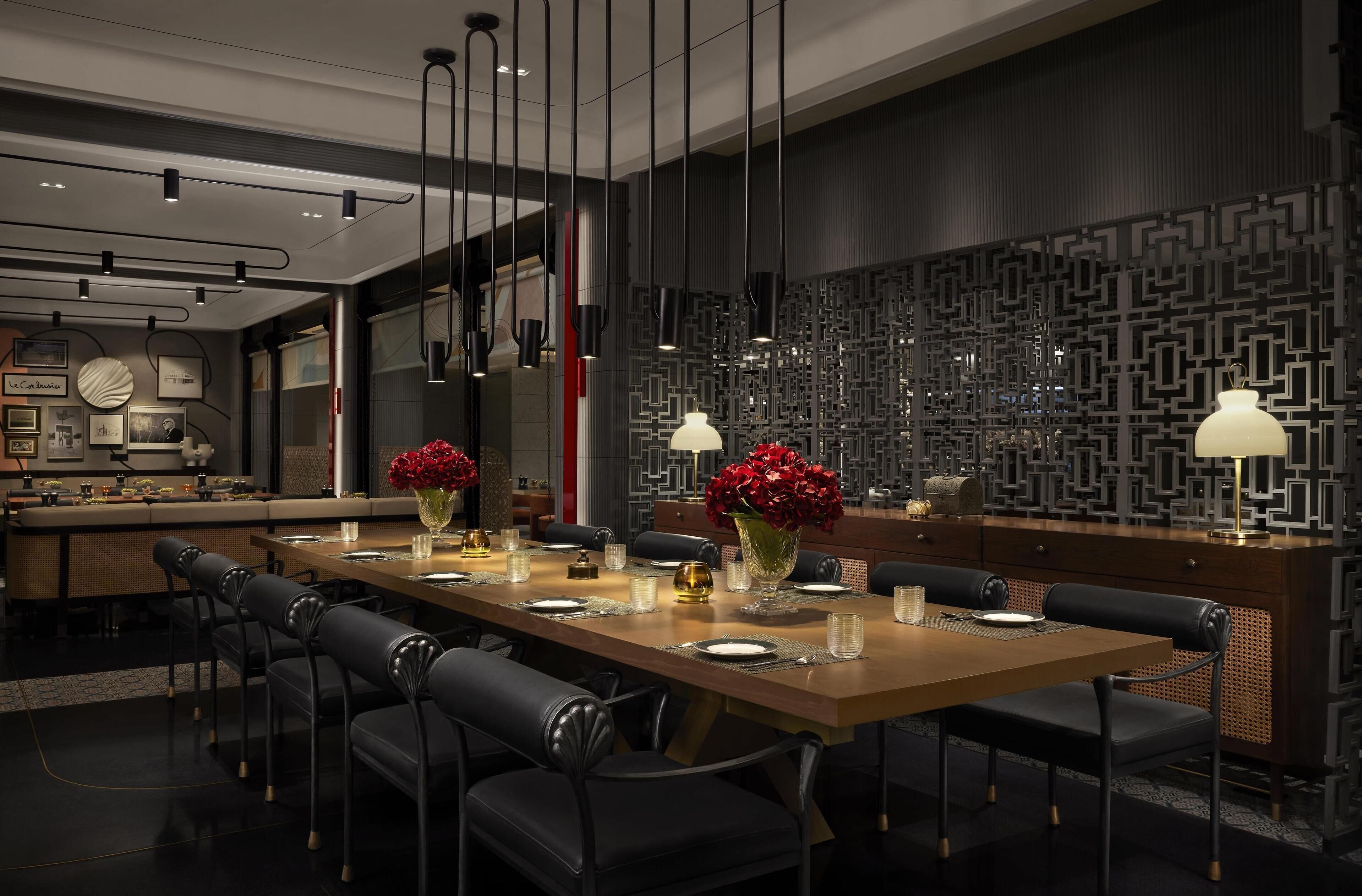 A modern dining area with a long wooden table, black upholstered chairs, and hanging pendant lights.