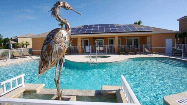 A swimming pool with a bird sculpture, a building with solar panels, and a fenced area with lounge chairs. - EV_1447 - 3 Bed, 3 Bath Townhome with Screened-In Private Pool and Access Resort (clermont)