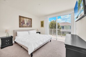 Relax in this serene bedroom with a large bed, nightstand, and TV, plus a sliding glass door leading to a balcony with a residential view.
