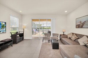 Relax in this inviting living space with a sofa, table, and entertainment unit, leading out to an outdoor area through a large glass door.