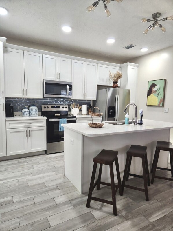 A modern kitchen with white cabinets, stainless steel appliances, a central island with stools, and a ceiling fan.