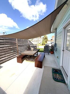 A patio with a wooden table and benches, a covered area, and a door to a building.
