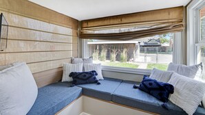 Eine Sitzecke mit gepolsterten Bänken und Kissen, ein Fenster mit Ausblick und eine Deckenleuchte.