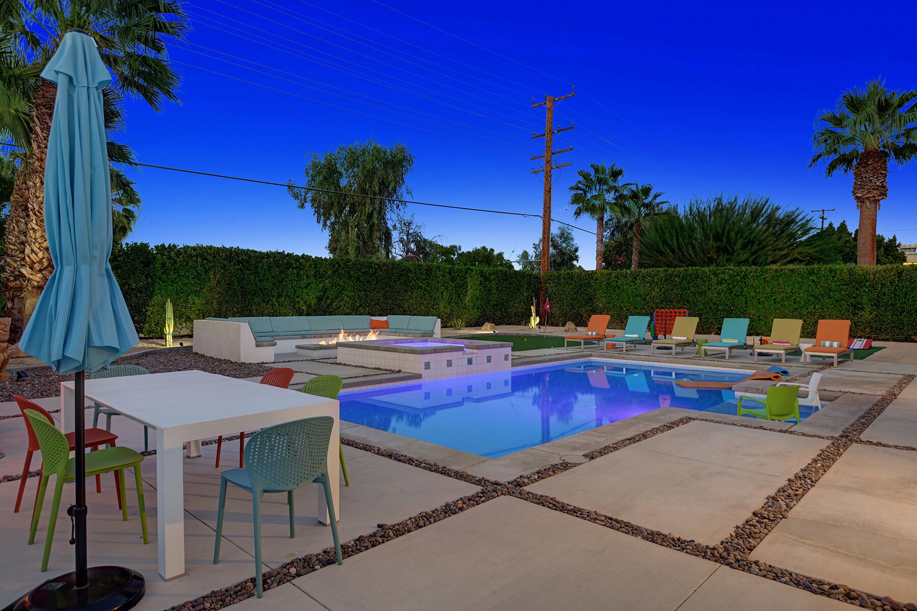 Zona de piscina con una pileta rectangular, sillas de descanso, una mesa y un paraguas azul.