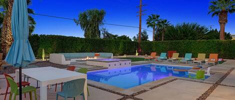 Zona de piscina con una pileta rectangular, sillas de descanso, una mesa y un paraguas azul.