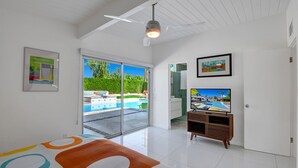 Un salon moderne doté d’un grand téléviseur, d’un ventilateur de plafond et offrant une vue sur une piscine grâce à des portes vitrées.
