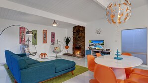 Un salon moderne avec un canapé bleu, des fauteuils orange, une cheminée en pierre et un téléviseur.