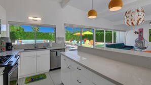 Une cuisine moderne dotée d’un grand îlot central, un coin repas avec vue sur une piscine, et un espace de vie comprenant un canapé et un fauteuil.