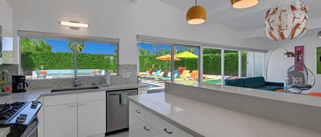 Une cuisine moderne dotée d’un grand îlot central, un coin repas avec vue sur une piscine, et un espace de vie comprenant un canapé et un fauteuil.