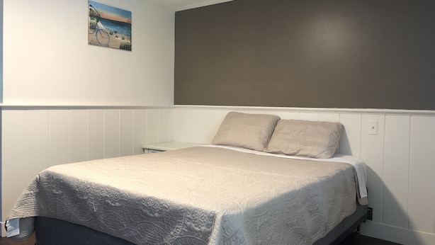 Una camera da letto con un letto, pareti bianche, una testiera grigia, un quadro raffigurante una spiaggia e un soffitto bianco.