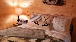 A cozy bedroom with a wooden interior, a bed with a quilt featuring bear and fern designs, and a wall-mounted basket with decorative items. - The Chalet is located in the woods of a gated property with a covered porch. (Darlington)