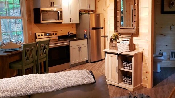 A cozy cabin interior with wooden walls, a kitchenette, a sofa with cushions, and a calendar on the wall. - The Chalet is located in the woods of a gated property with a covered porch. (Darlington)