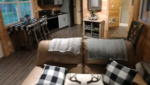 A cozy cabin interior with a leather sofa, checkered pillows, a mirror, and a sign reading "Stay awhile". - The Chalet is located in the woods of a gated property with a covered porch. (Darlington)