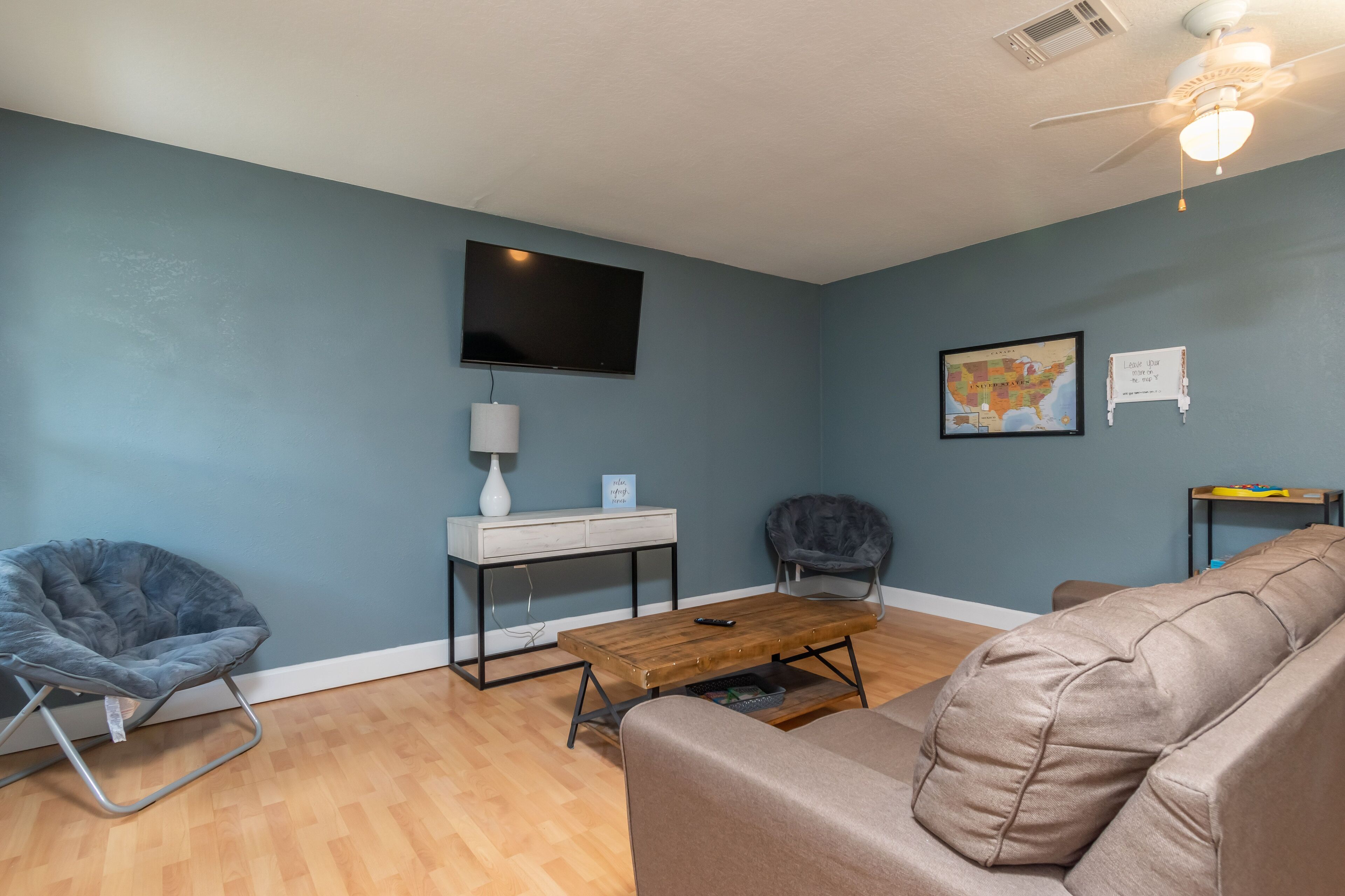 A living room with a flat-screen TV, a map, a desk with a lamp, and a sofa.