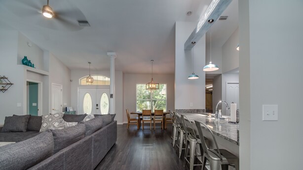 A modern living room with a gray sectional sofa, a dining area with a wooden table and chairs, and a kitchen with a marble countertop and bar stools. - HEATED PRIVATE POOL | CLOSE TO RAINBOW RIVER, CRYSTAL RIVER & GOLFING (Citrus Springs)