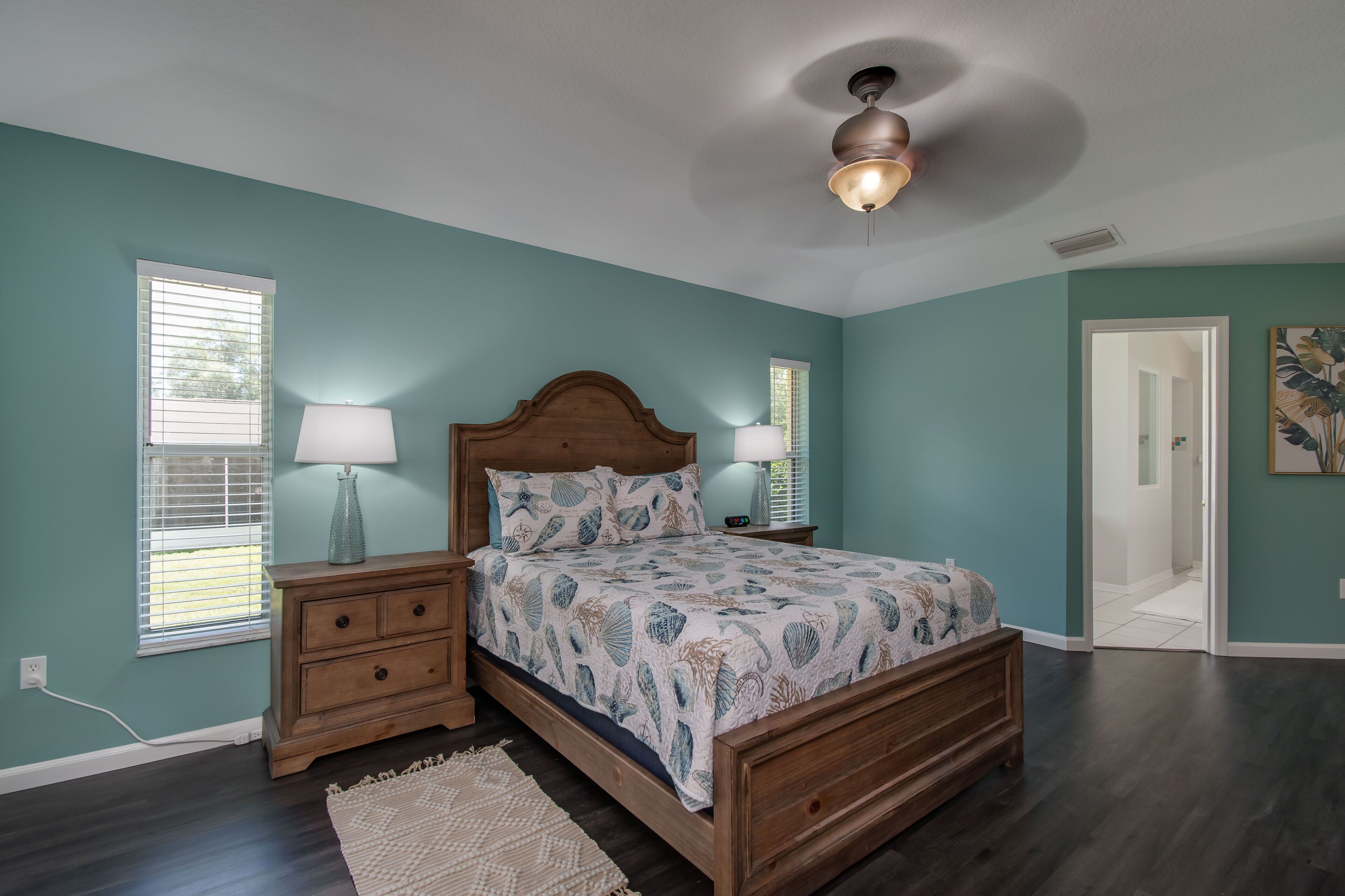A bedroom with teal walls, a wooden bed, two bedside tables with lamps, and a ceiling fan.