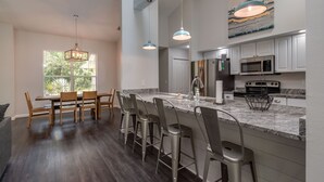 A modern kitchen with a large island, bar stools, and a dining area with a wooden table and chairs. - HEATED PRIVATE POOL | CLOSE TO RAINBOW RIVER, CRYSTAL RIVER & GOLFING (Citrus Springs)