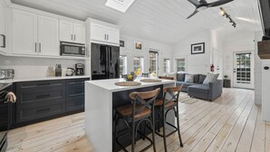 A modern kitchen with white cabinetry, a large island, and a dining area with bar stools. - The Cambridge Cove! Hot tub & Outdoor Gas Firepit (Fort Erie)
