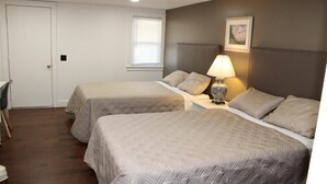Une chambre d’hôtel avec deux lits, un bureau, une chaise, une lampe et une fenêtre avec des stores.