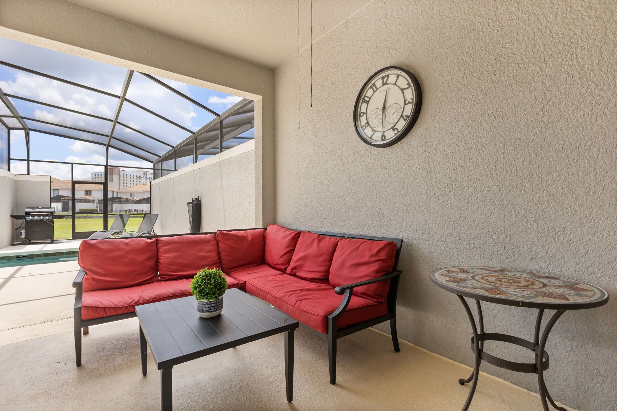 Un espacio de patio cubierto con un sofá rojo, una mesita y un reloj en la pared.