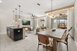 A modern kitchen with a central island, dining area with a large table and chairs, and a living space with a sofa and a television.