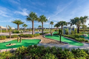 A golf course with multiple green lawns, palm trees, and a clear blue sky.