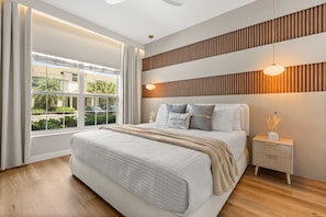 A bedroom with a large bed, a nightstand, a bedside lamp, and a window with curtains.