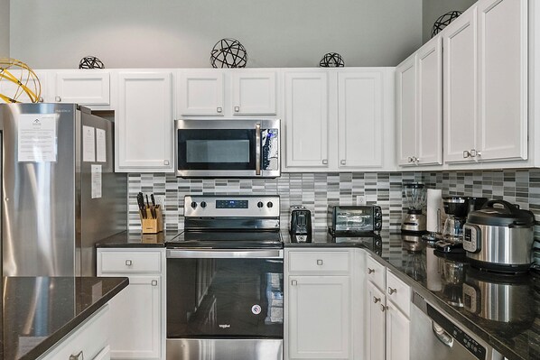 Una cocina moderna con gabinetes blancos, electrodomésticos de acero inoxidable y un salpicadero de azulejos.