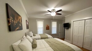 Une chambre avec deux lits, un ventilateur de plafond, une télévision et une porte.