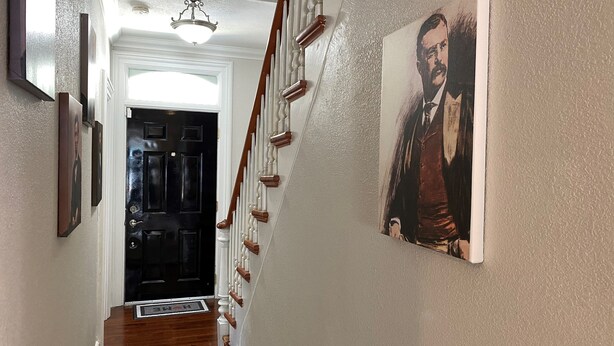 Un couloir avec une porte noire, un escalier en bois et un luminaire au plafond.