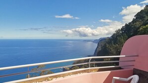 En balkon med udsigt over havet og en rosa væg.