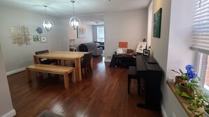 Een ruime woonkamer met een houten eettafel, een zwarte bank en een piano.