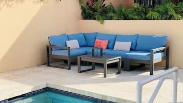 A swimming pool with a tiled edge, a white pool ladder, and a blue sofa with cushions.