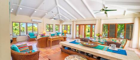 A spacious room with a high ceiling, large windows, and a central dining area with a long table.