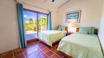 A room with two beds, a ceiling fan, a painting of a beach scene, and a view of palm trees through the glass door.