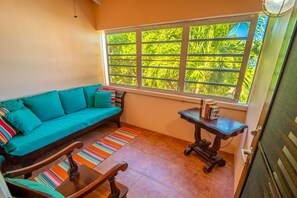 Una habitación acogedora con un sofá color turquesa, una pequeña mesa de madera y una ventana con vistas a zonas verdes.