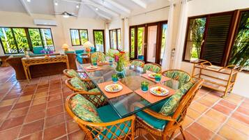 A spacious dining area with a glass table, wicker chairs, and a view of the outdoors through large windows.