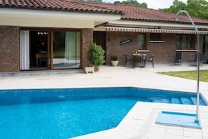 Ein Schwimmbecken mit Fliesenbord, eine überdachte Terrasse mit Gartenmöbeln und ein Backsteinhaus mit der Aufschrift "SEAFARER".